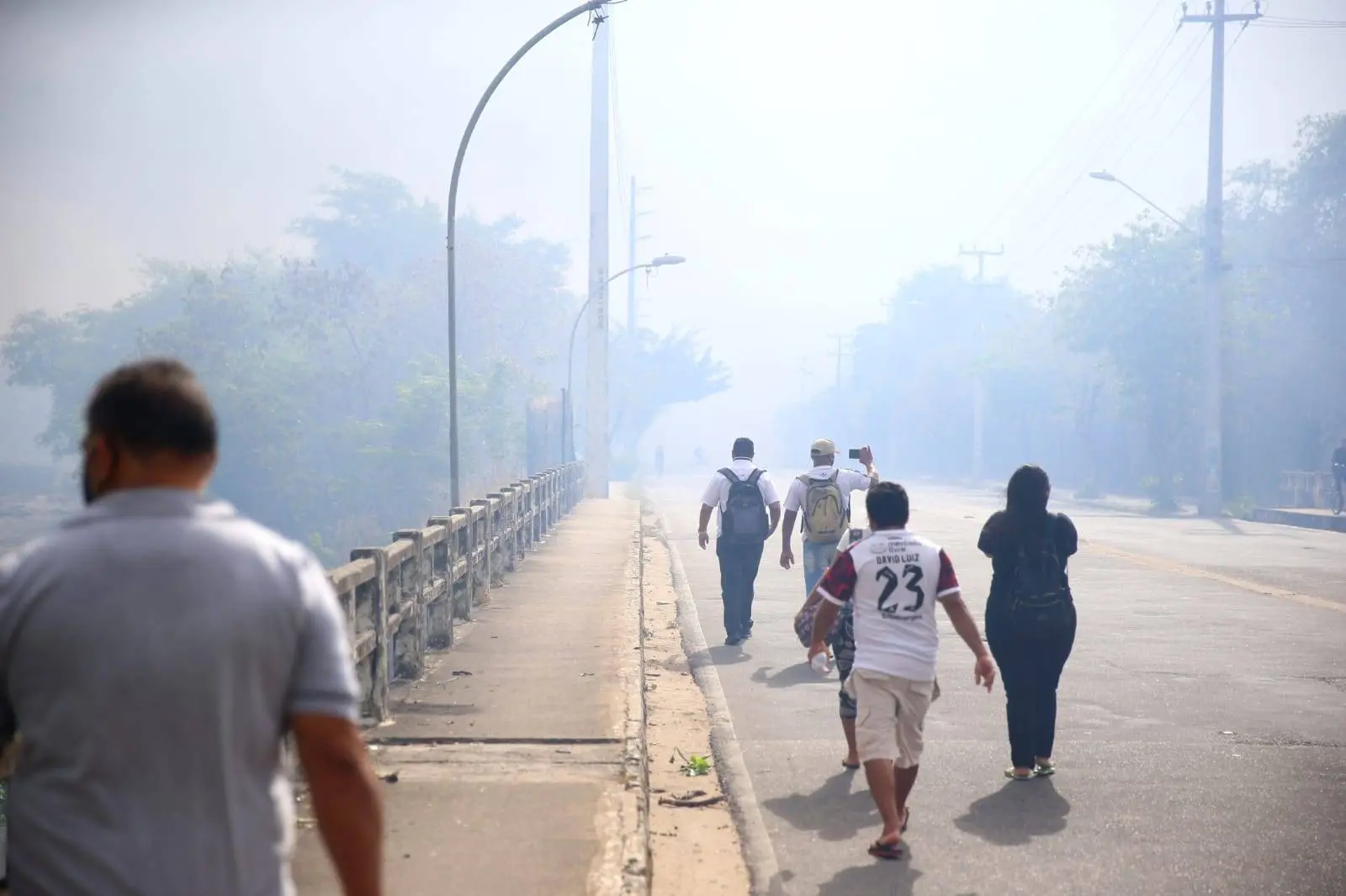 Pessoas passando em fonte sob fumaça de ncêndio no Parque do Cocó, em Fortaleza
