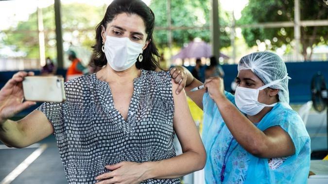 Mulher tirando selfie ao receber vacina contra Covid-19 em Fortaleza, no Ceará