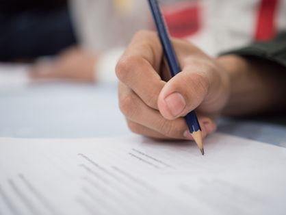 Close-up em uma mão escrevendo a lápis em um documento escolar