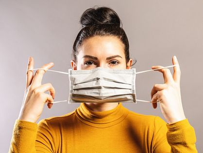 Imagem mostra mulher colocando uma máscara cirúrgica no rosto.