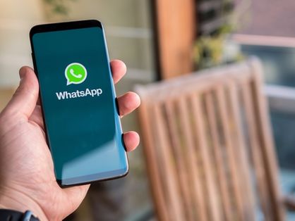 A imagem mostra uma mão segurando um celular aberto no aplicativo WhatsApp.