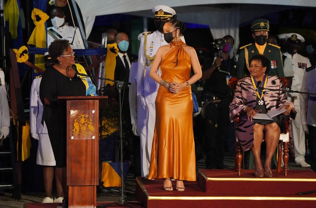 A cantora Rihanna está num palco, vestida de dourado, recebendo o título de 