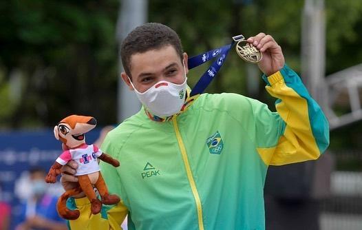 Skatista cearense Lucas Rabelo segura mascote dos  Jogos Pan-Americanos Júnior de Cali na mão direita e a medalha de ouro na mão esquerda
