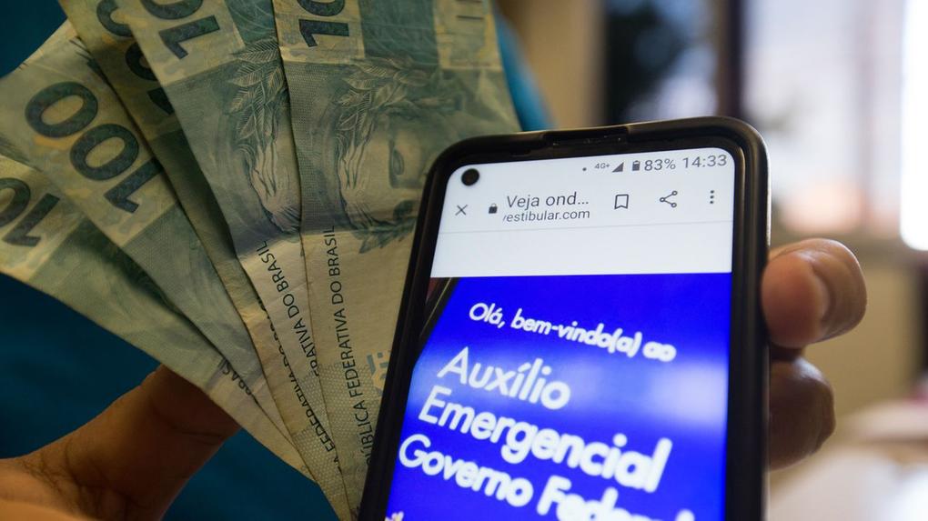 Dinheiro e celular aberto no app do auxílio emergencial