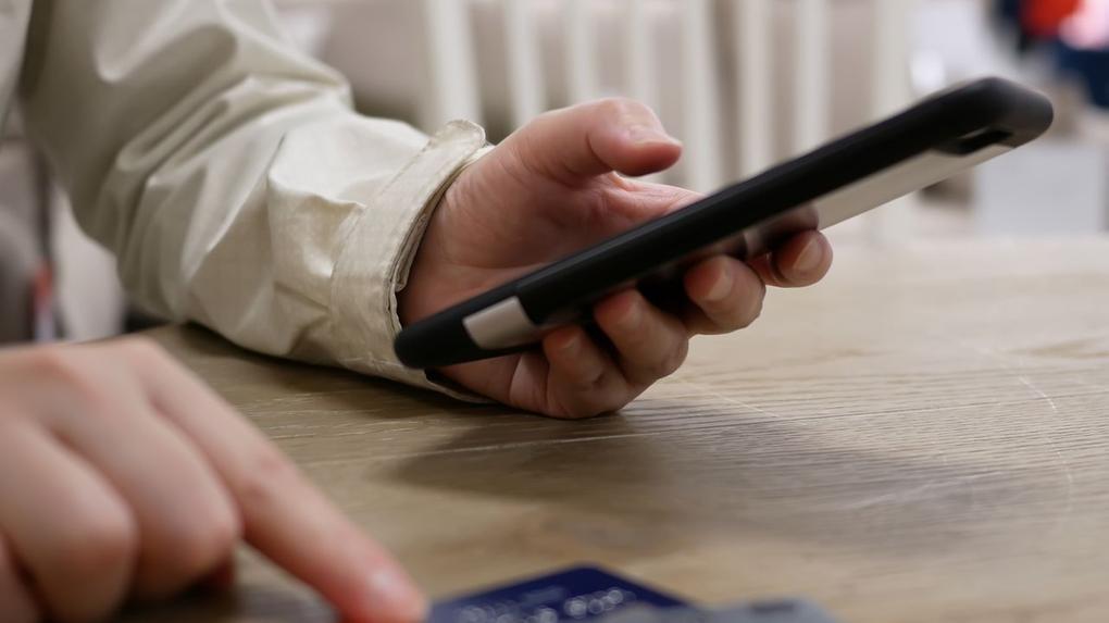 A imagem mostra uma pessoa segurando um celular com uma das mãos e mexendo em cartões de crédito com a outra.