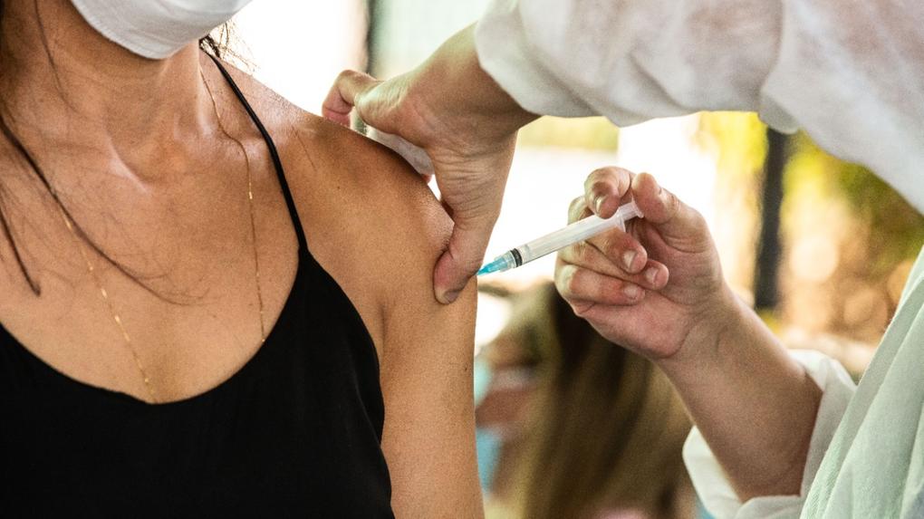 A imagem mostra uma pessoa aplicando vacina no braço de uma mulher.