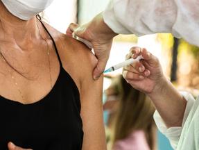 A imagem mostra uma pessoa aplicando vacina no braço de uma mulher.