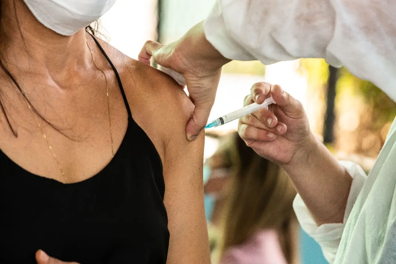 A imagem mostra uma pessoa aplicando vacina no braço de uma mulher.