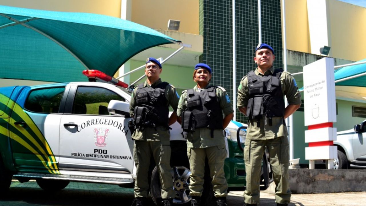 Três agentes da Polícia Militar do Piauí, dois homens e uma mulher, posam enfrente a uma viatura da Corregedoria