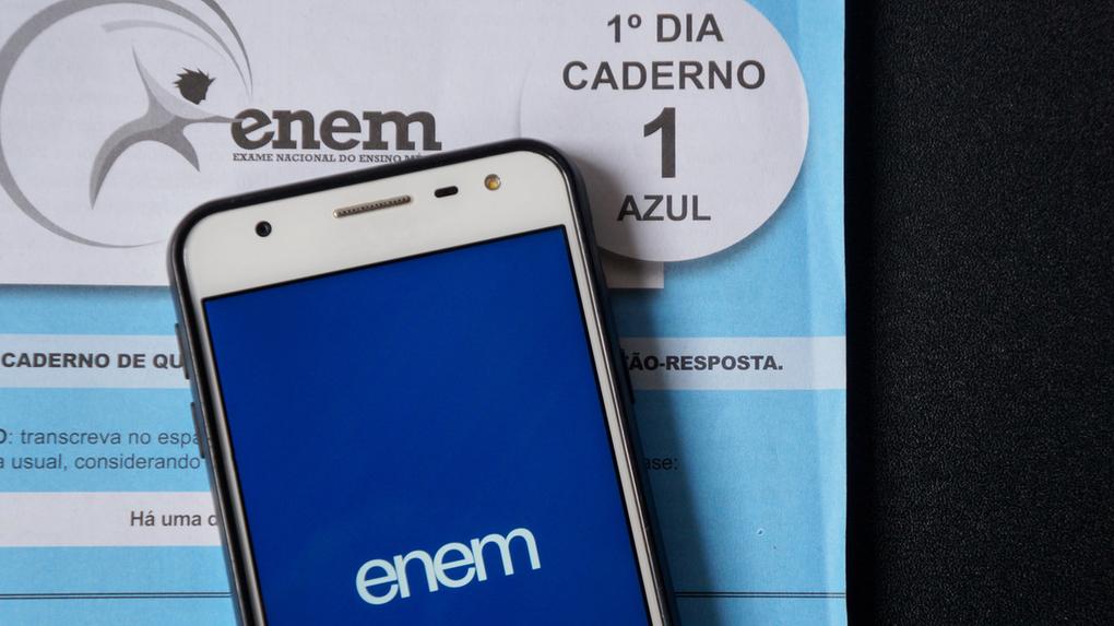 Aplicativo ENEM na tela de um smartphone em cima de um teste azul do ENEM em fundo preto