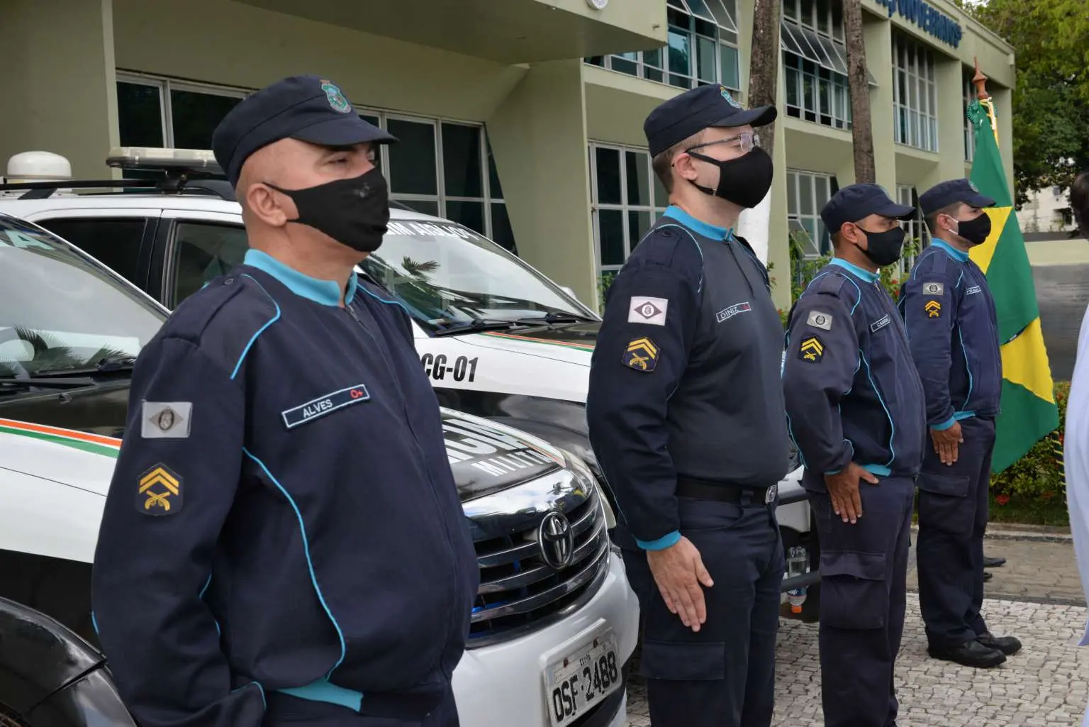 policiais militares, lado a lado, diante de viaturas