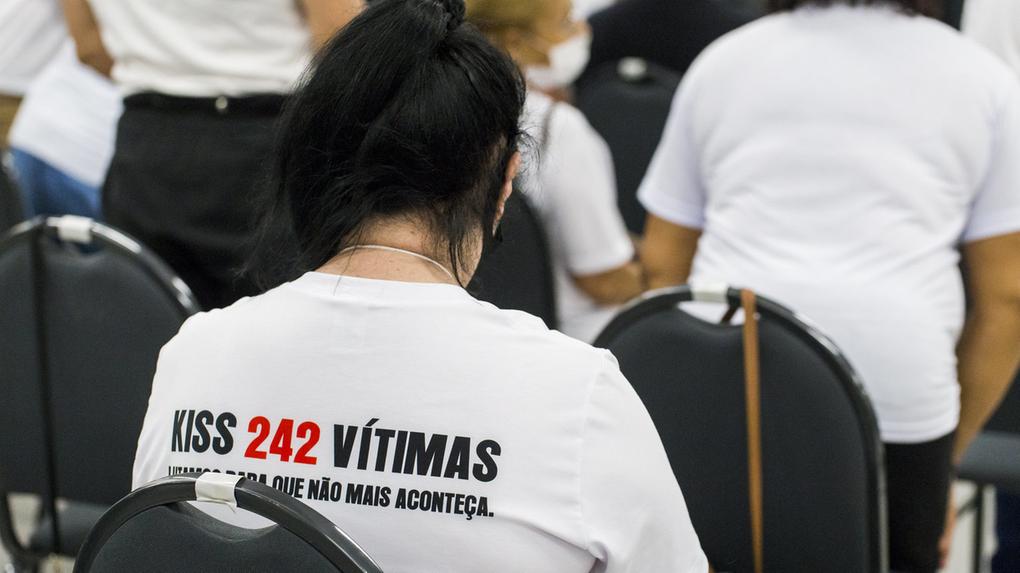 Pessoa usa blusa branca com escritos nas costas que diz Kiss 242 vítimas