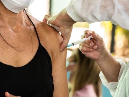 A imagem mostra uma pessoa aplicando vacina no braço de uma mulher