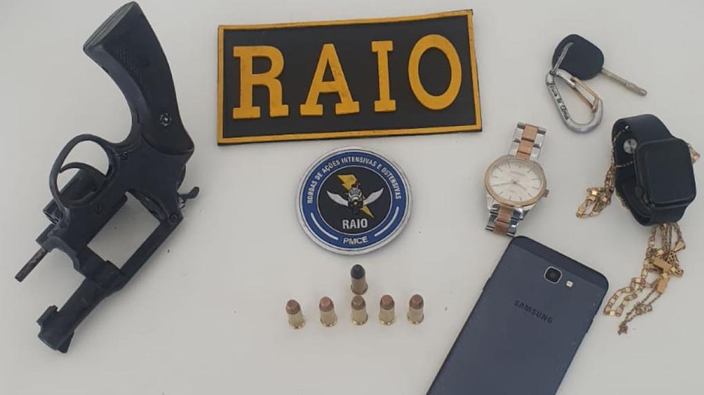 ama, munições, celular, relógio e objetos em uma mesa com a placa do raio da PMCE