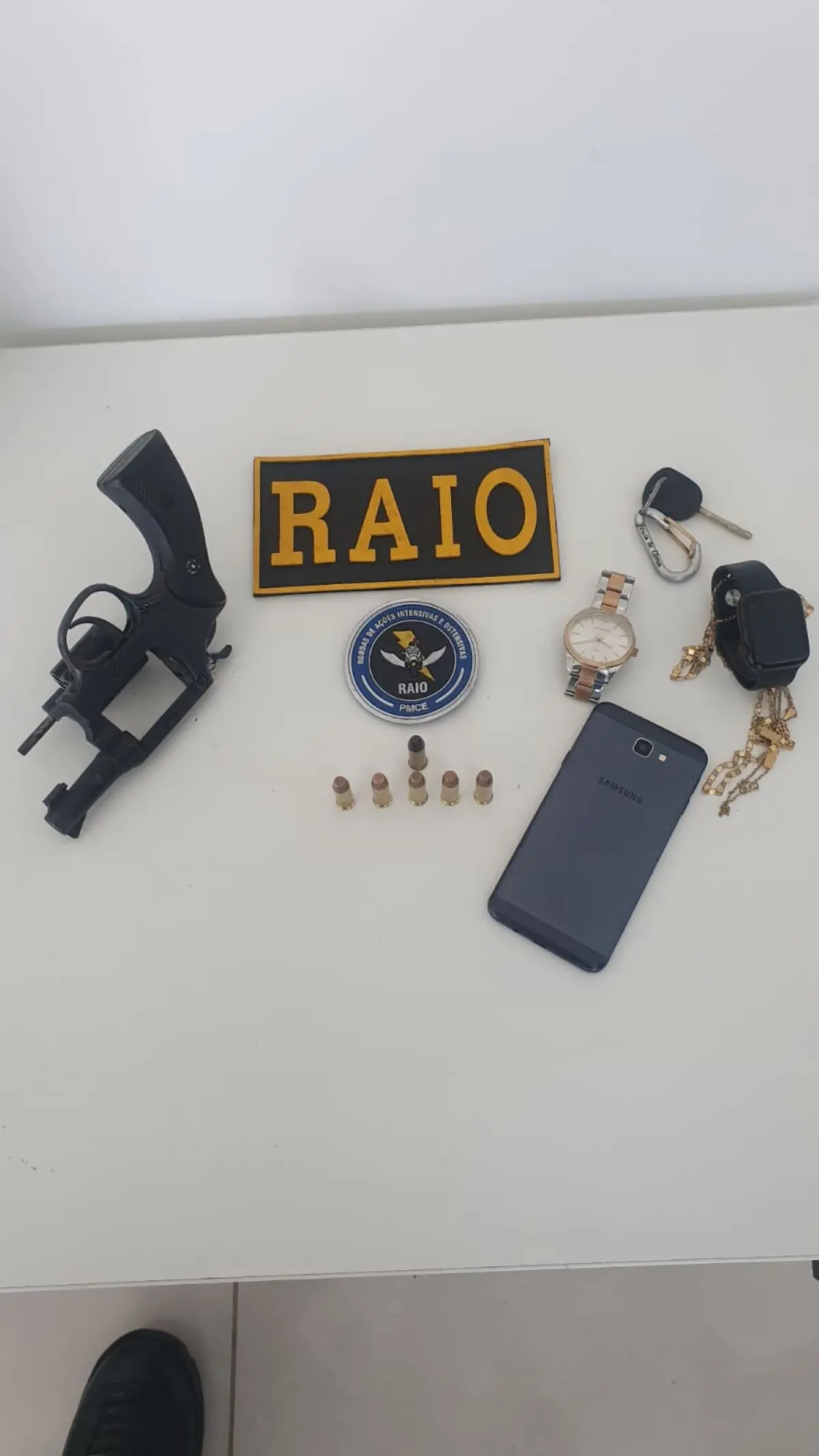 ama, munições, celular, relógio e objetos em uma mesa com a placa do raio da PMCE