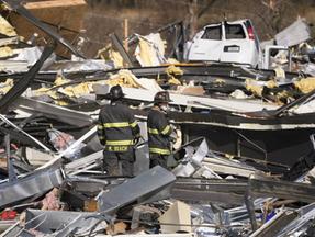 Dois bombeiros vasculham os escombros de uma fábrica destruída por tornados em Mayfield.