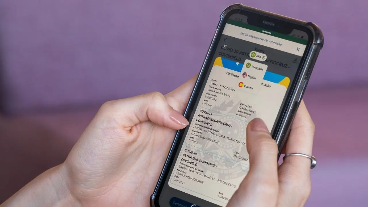 Uma mão segurando um celular mostrando o certificado nacional de vacinação contra a Covid-19.