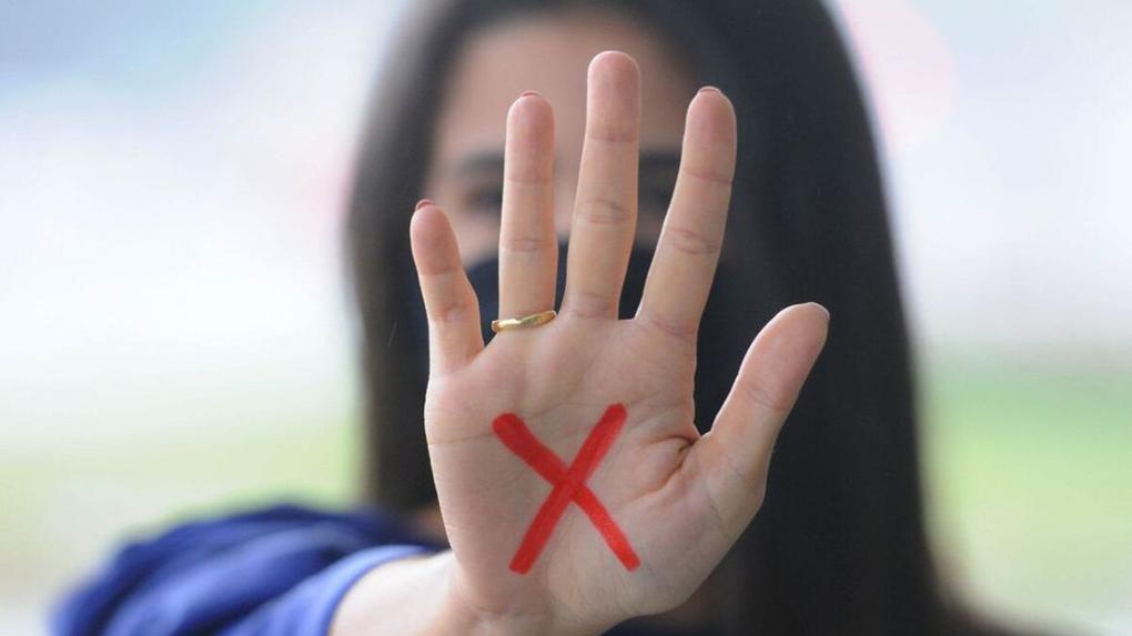 Mulher com letra X desenhada em tinta vermelha na mão, como pedido de socorro contra violência