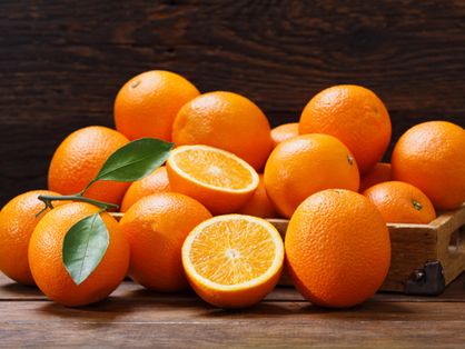 Frutas frescas de laranja com folhas em uma caixa na mesa de madeira
