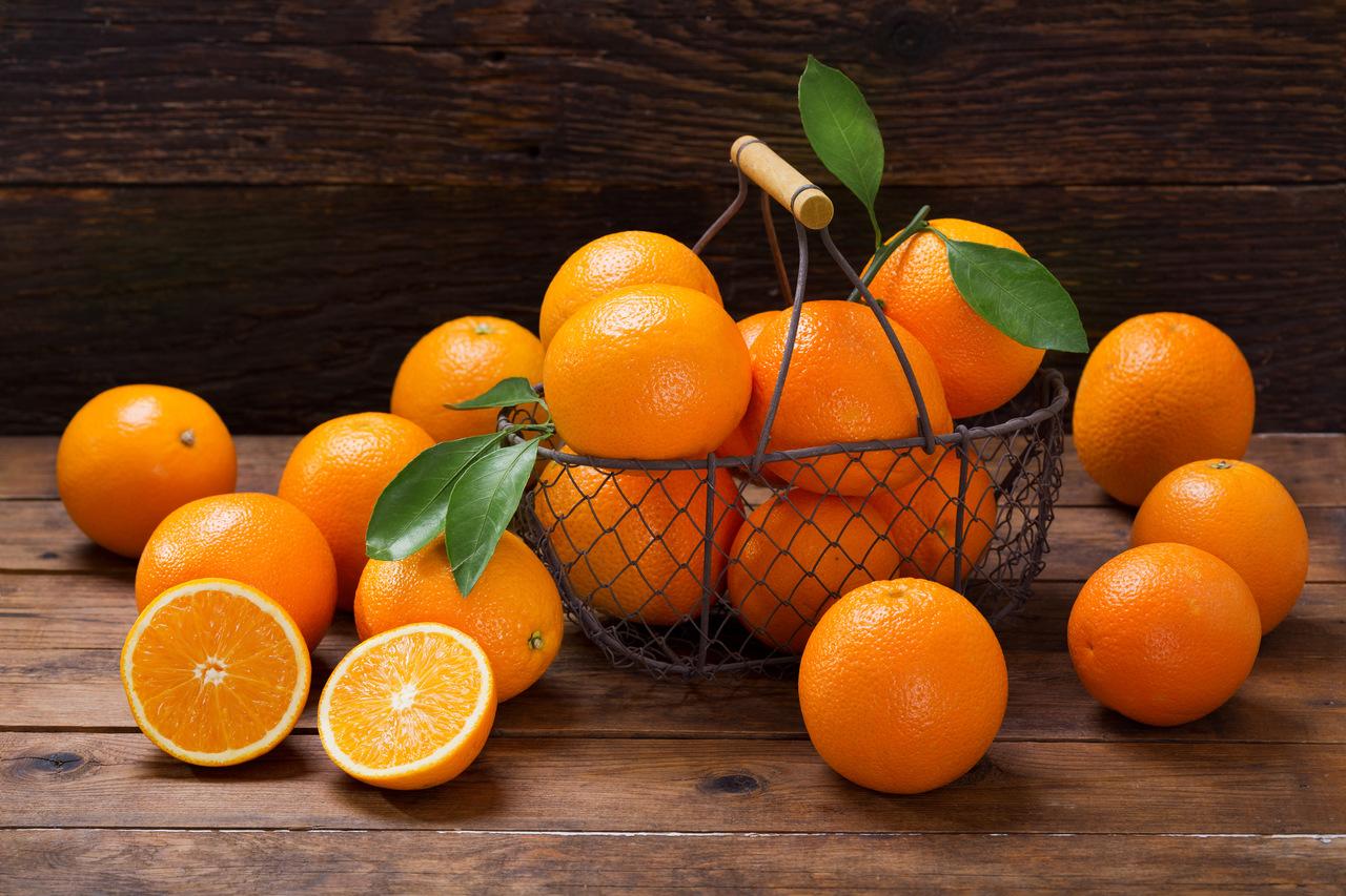 Frutas frescas de laranja com folhas em uma cesta na mesa de madeira