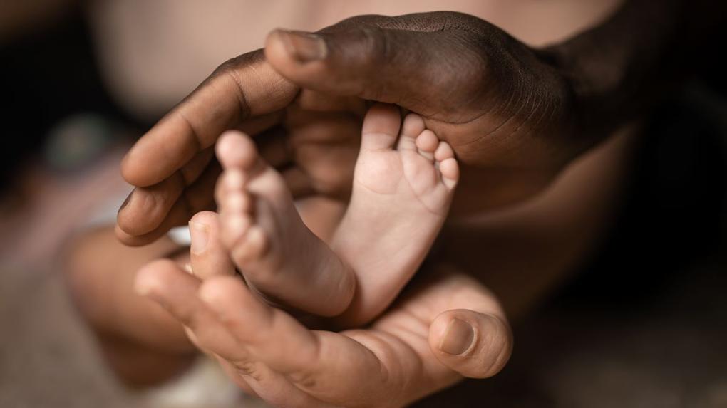 mão de uma pessoa negra segurando os pés de um recém-nascido