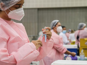 profissional de saúde, trajando jaleco rosa, prepara injeção de vacina