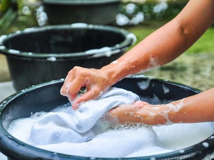 Foto mostra pessoa lavando roupa branca em uma bacia preta