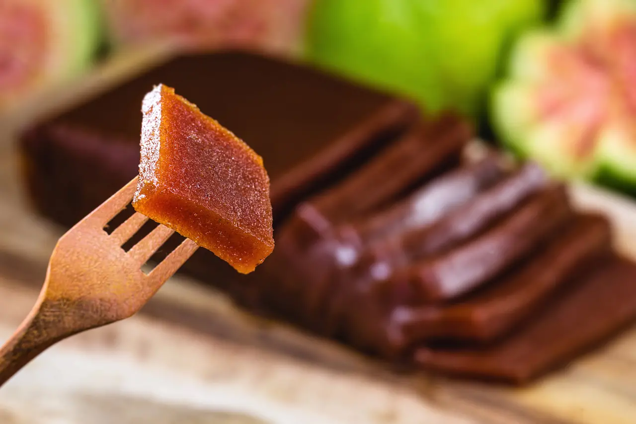 Pedaço de doce de goiaba em um garfo de madeira rústico. Goiaba turva ao fundo.