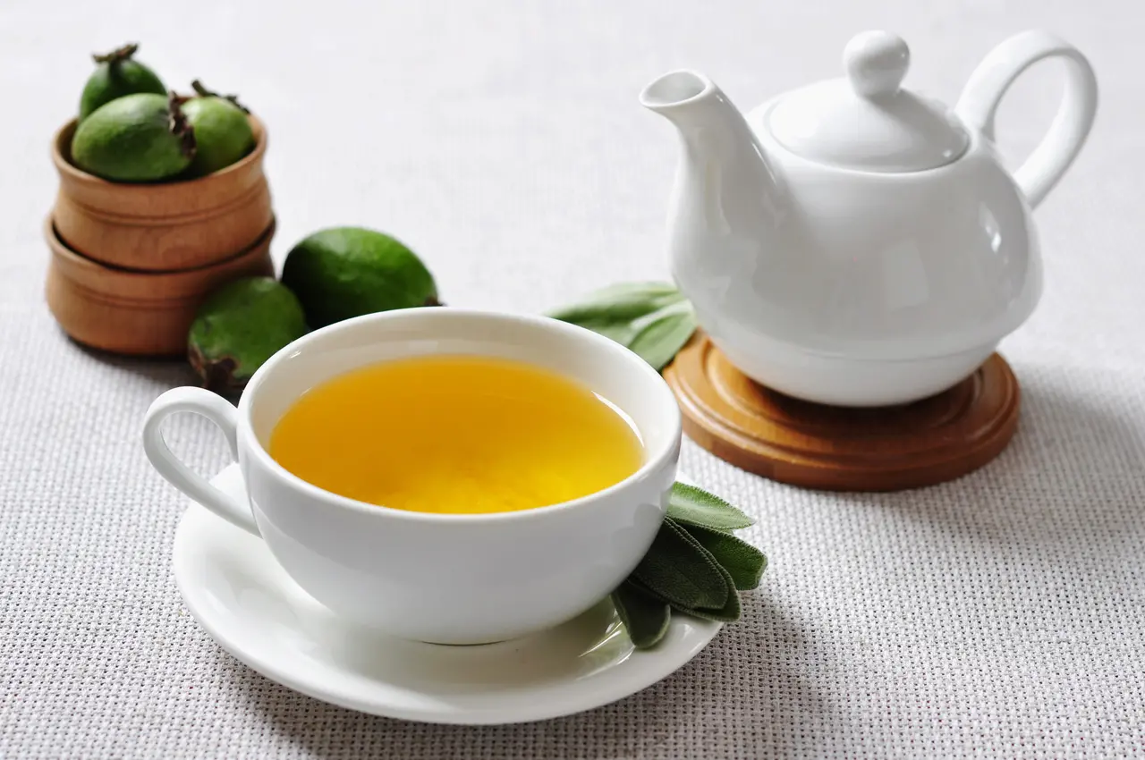 Xícara de chá de ervas e goiaba ao lado de uma chaleira e uma tigelas de madeira com goiabas maduras