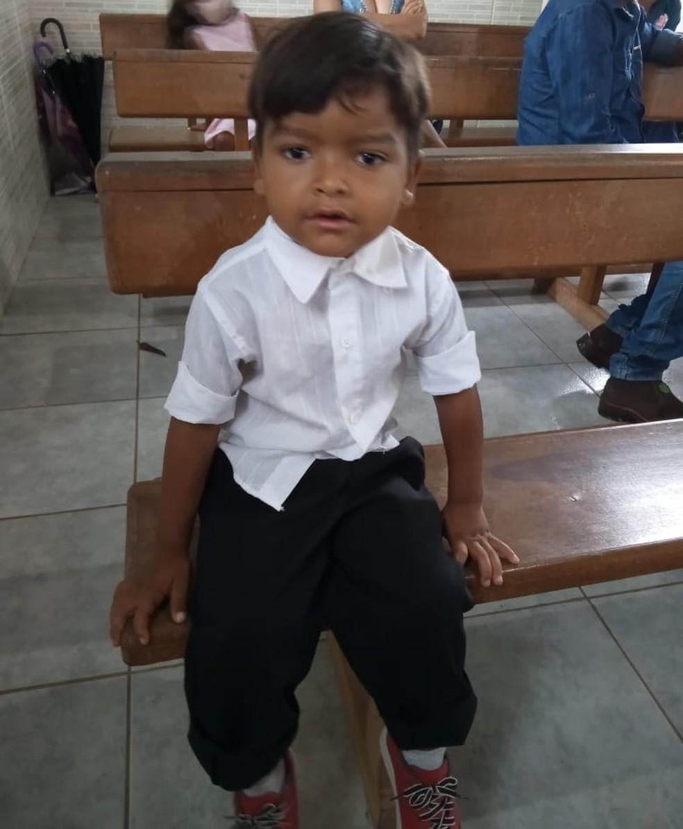 Menino de blusa branca sentado em um banco de igreja