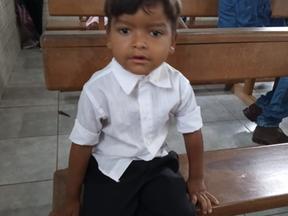 Menino de blusa branca sentado em um banco de igreja