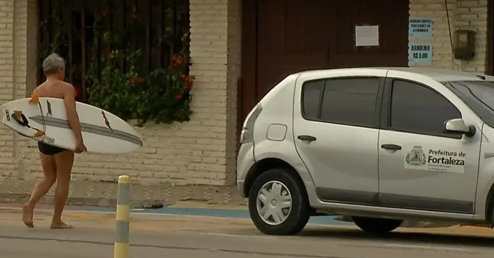Homem atravessa a rua com uma prancha embaixo dos braços