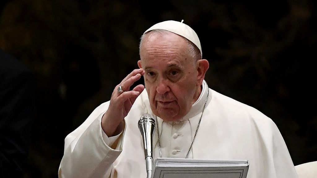 Papa Francisco com mão erguida em frente a púlpito com microfone