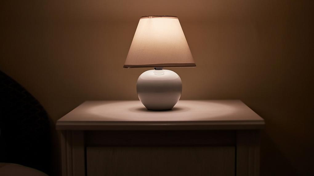Uma pequena lâmpada brilhando na mesa de cabeceira do quarto, sala escura