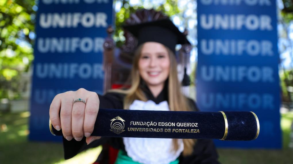 Graduanda com beca mostrando canudo com diploma