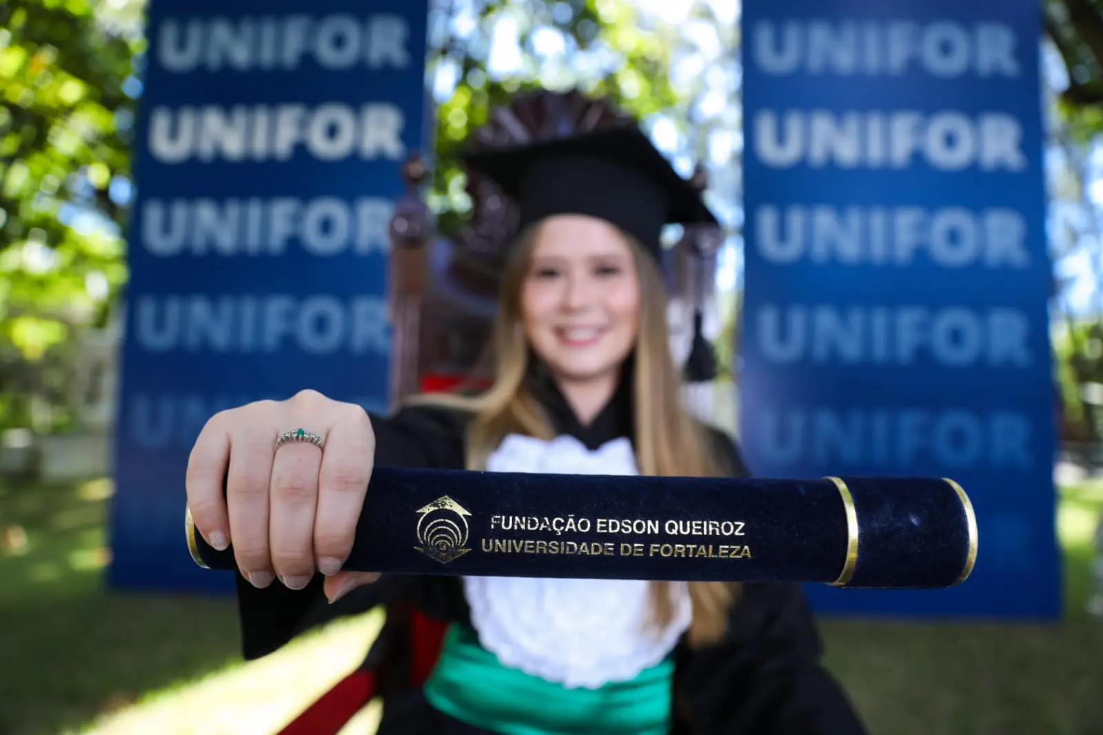Graduanda com beca mostrando canudo com diploma
