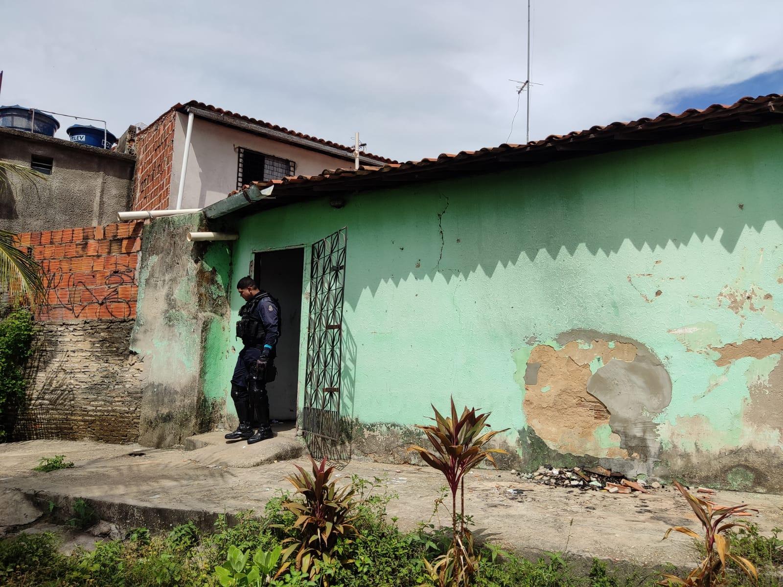 Casa simples com parede verde e portão de grade preta usada como cativeiro. Na imagem, há um policial na entrada do imóvel