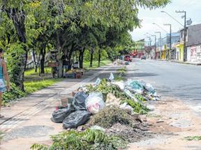 A imagem mostra uma mulher caminhando na calçada ao lado de um ponto de lixo em Fortaleza.