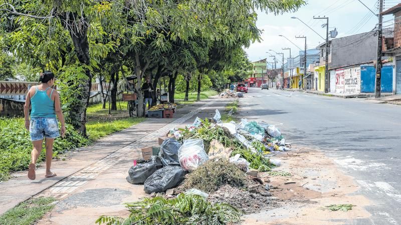 A imagem mostra uma mulher caminhando na calçada ao lado de um ponto de lixo em Fortaleza.
