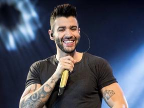 Gusttavo Lima sorrindo com microfone na mão durante show