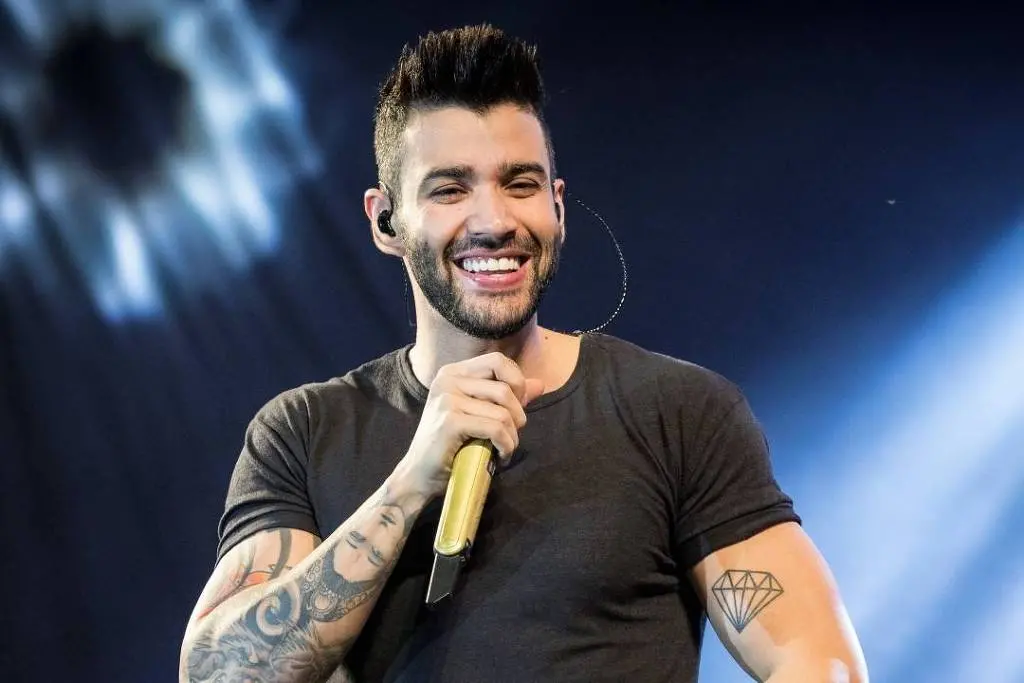 Gusttavo Lima sorrindo com microfone na mão durante show