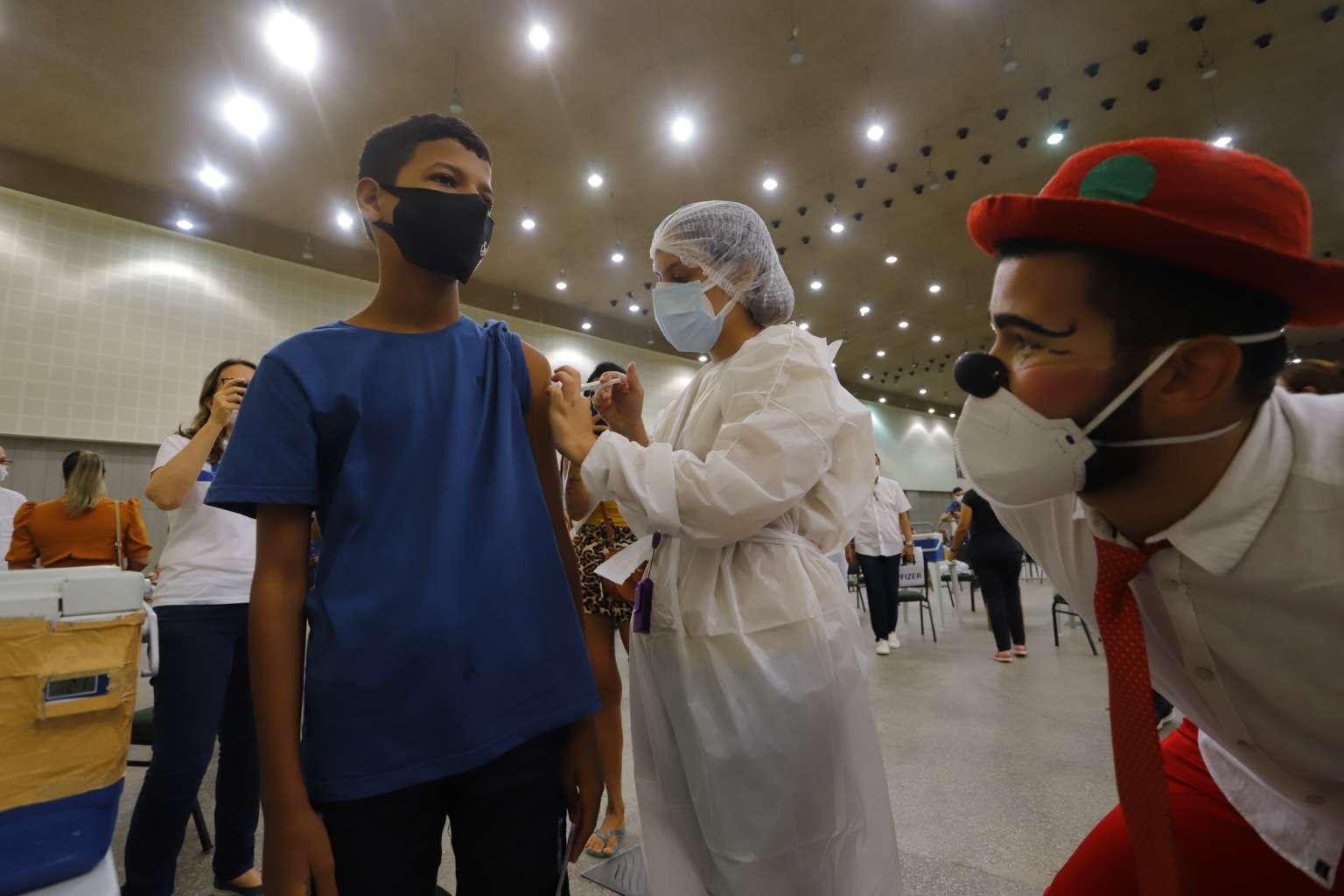 Criança é vacinada contra Covid em Fortaleza sob olhar de um palhaço