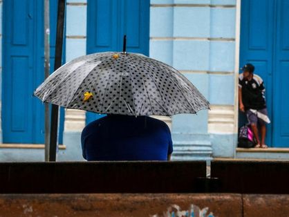 Sentado em um banço de praça, homem segura guarda-chuvas