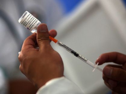Mão de profissional de saúde retirando dose de vacina de frasco com seringa