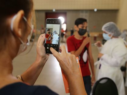 mulher segura celular e fotografa menino sendo vacinado contra a covid-19