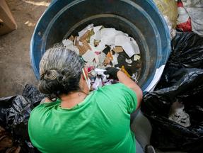 Mulher mexe em um cesto de lixo em busca de materiais recicláveis.