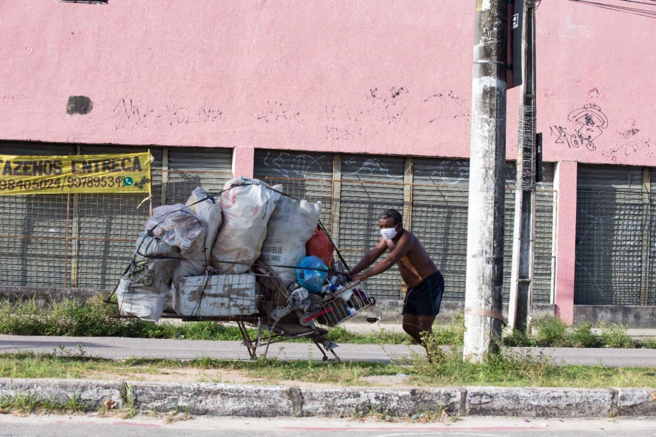 Catador de resíduos recicláveis empurra um carrinho com materiais recolhidos em uma avenida de Fortaleza.