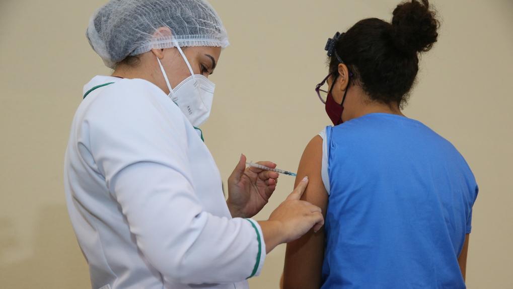 Profissional aplica vacina contra a Covid em criança de costas