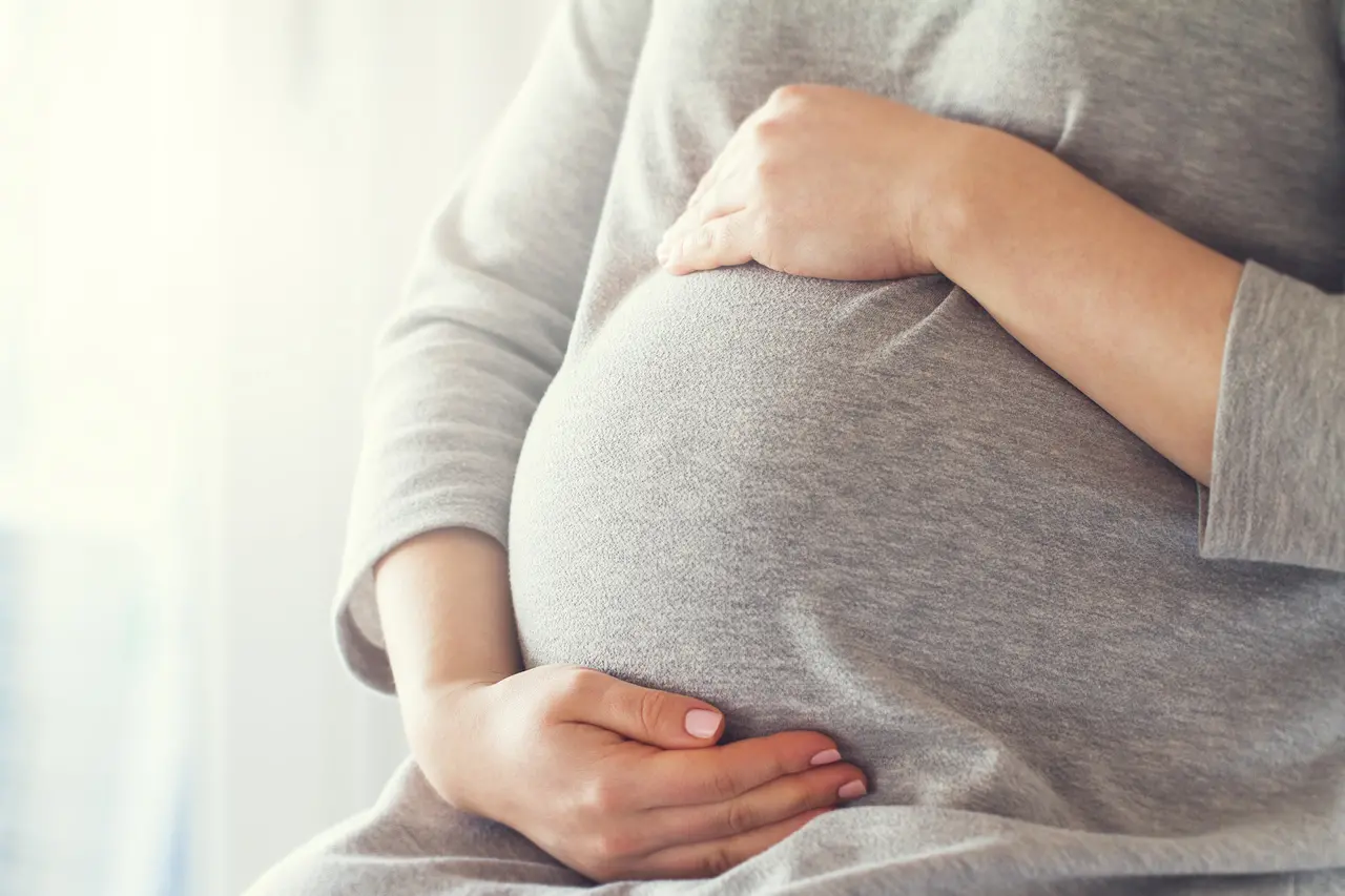 Gestante usando roupa cinza apoia mãos na barriga