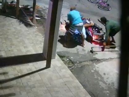motociclista caído no chão e assaltantes ao redor dele. um dos homens carrega um facão e uma enxada